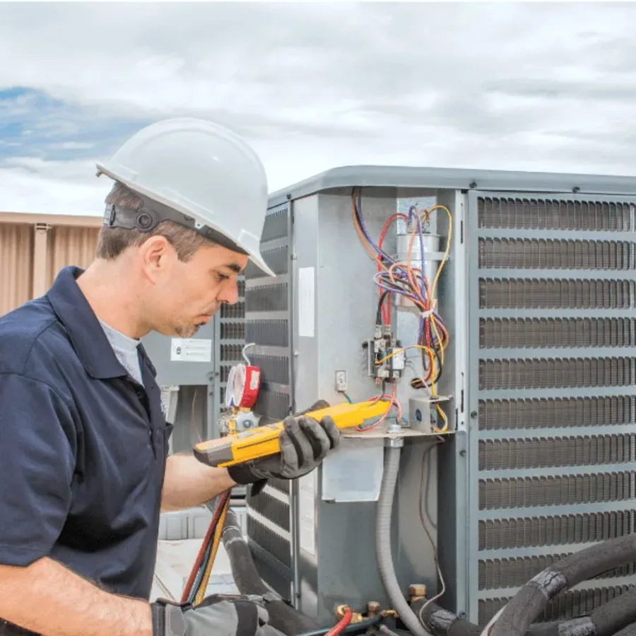 HVAC technician in a hard hat testing an outdoor air conditioner with a multimeter